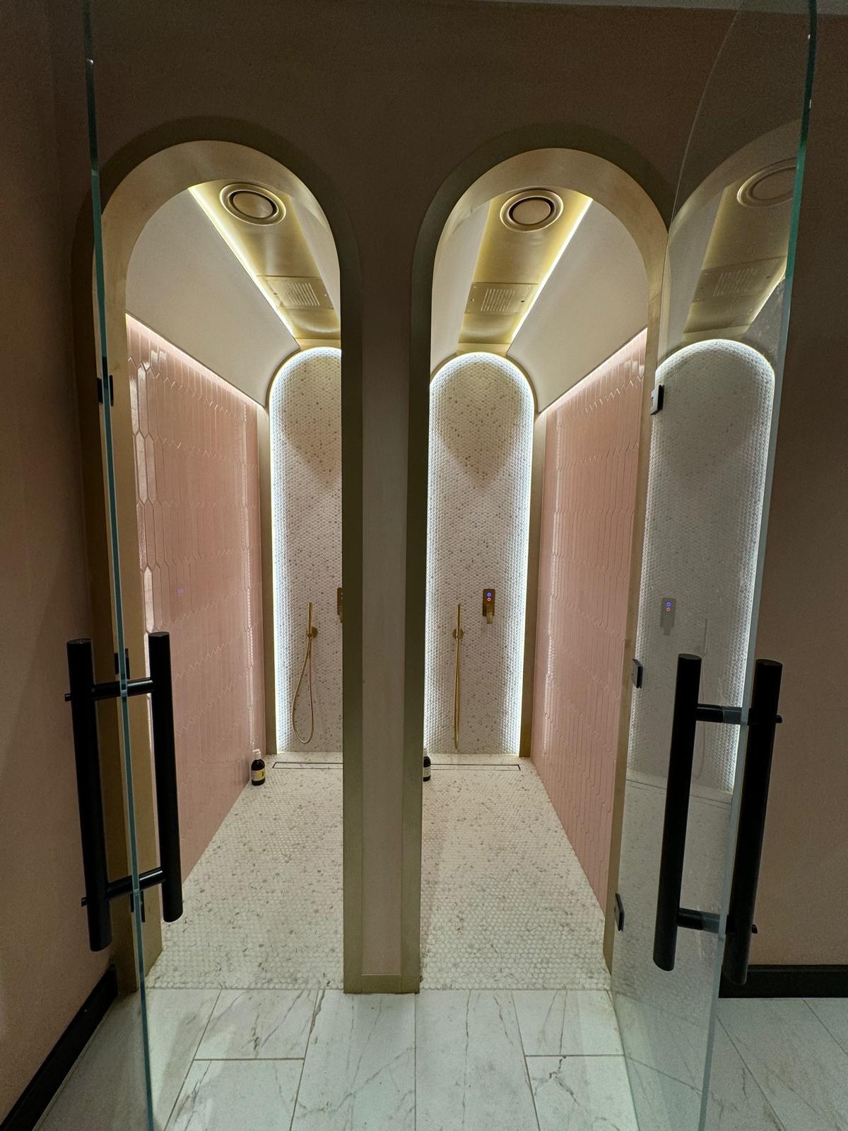 Twin shower stalls with pink hex tile and gold-trimmed arches