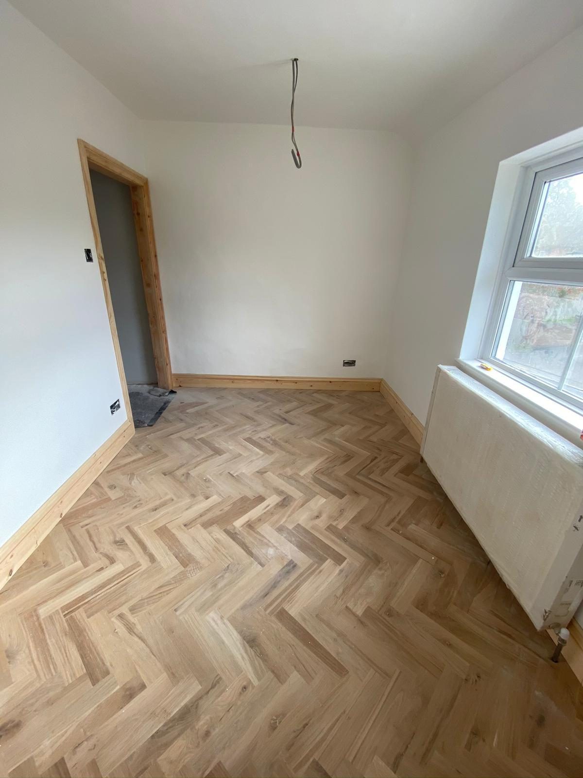 Newly laid herringbone wood floor in a freshly painted room by Centaurus Construction
