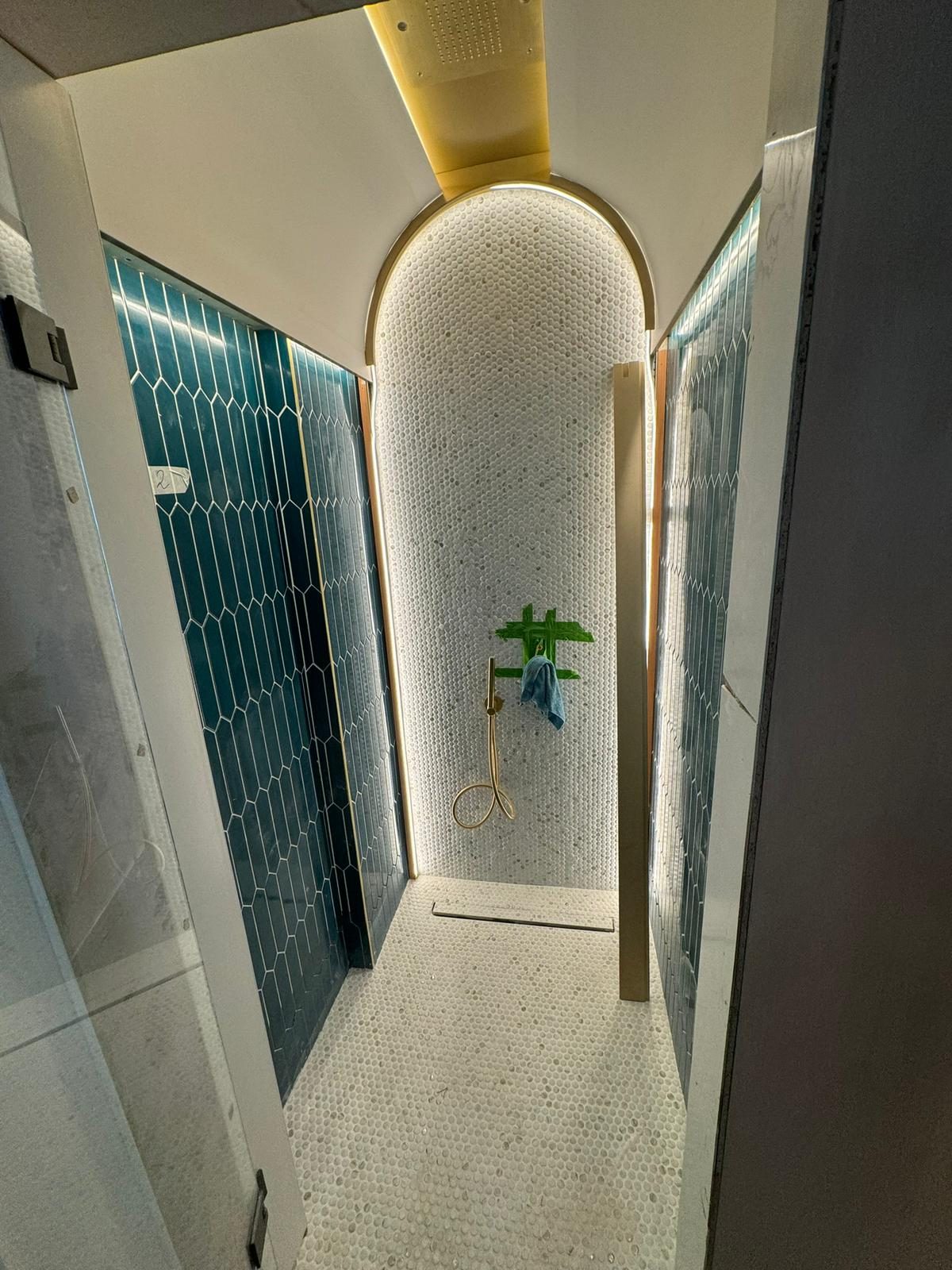 Walk-in wet room with teal hex tile and a brass rain shower